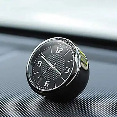 Close-up of a mini analog car dashboard clock featuring a black dial and sleek silver rim, resting securely on a textured car interior surface.