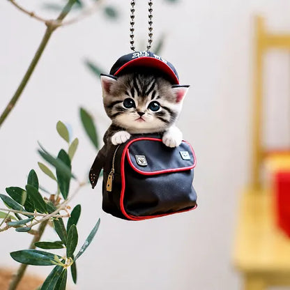 A cute backpack cat car interior hanging accessory suspended by its chain from an indoor plant branch, showing its versatile decorative use beyond the vehicle.