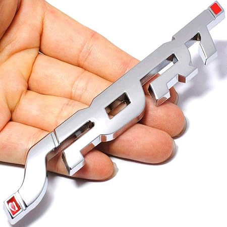 Metallic car emblem held in a hand against a white background