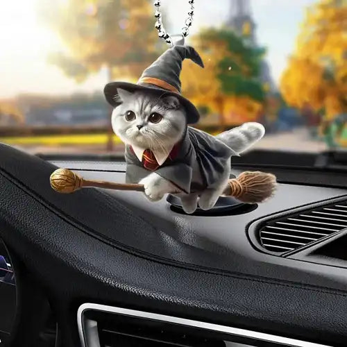 A cute wizard cat wearing a hat and cape while riding a broomstick, functioning as a rearview mirror charm hanging inside a car over the dashboard.