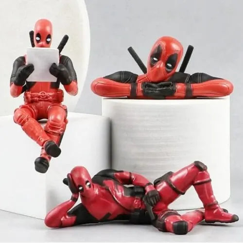 A collection set of three Deadpool car dashboard figures displayed on white podiums. The set features the superhero in three distinct poses: sitting and reading, leaning forward on his arms, and lying down in a relaxed pose.