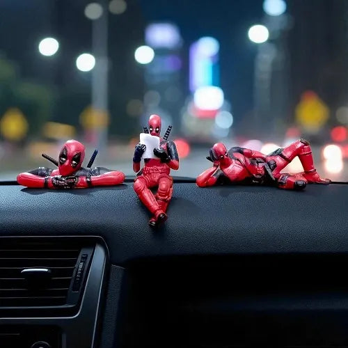 All three Deadpool superhero car dashboard accessories mounted together on a vehicle's dashboard, beautifully photographed against a cinematic background of blurred urban city night lights.
