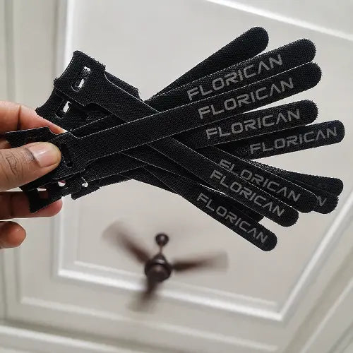 A hand holding a fanned-out group of black Florican branded reusable velcro cable ties, designed for easy cord organization and home office wire management.