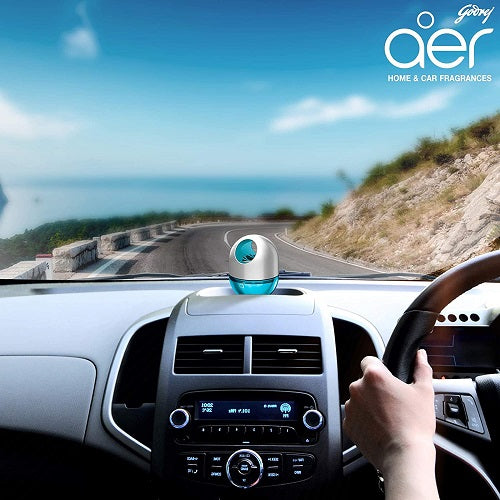 Car interior with a dashboard fragrance diffuser, scenic road in the background, and 'aer' brand logo.