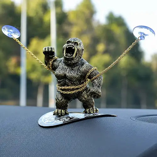 A gold King Kong gorilla dashboard accessory standing on a black base, secured to the car's interior using two clear windshield suction cups attached to its gold chains.