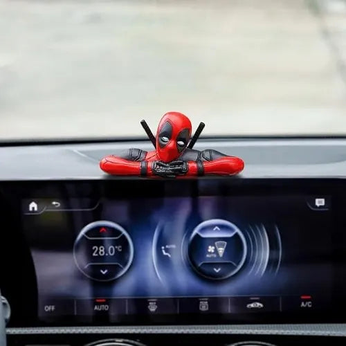 The leaning Deadpool car ornament mounted cleverly on top of the vehicle's central infotainment screen display, looking forward into the cabin over the digital climate controls.