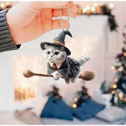 A person holding a magic cat on a broomstick car hanging ornament by its metal bead chain, showing the detailed craftsmanship of the wizard outfit against a softly lit indoor background.