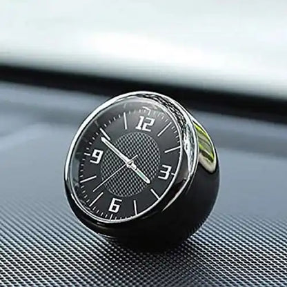 Close-up of a mini analog car dashboard clock featuring a black dial and sleek silver rim, resting securely on a textured car interior surface.