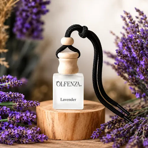 Close-up of the Olfenza Lavender hanging car air freshener with a wooden cap and black cord, resting on a wooden display block surrounded by vibrant purple lavender sprigs.