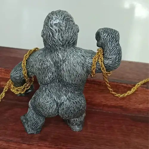Back view of the silver gorilla car showpiece resting on a wooden surface, showing the detailed fur sculpting and how the gold chain wraps around its muscular arms.