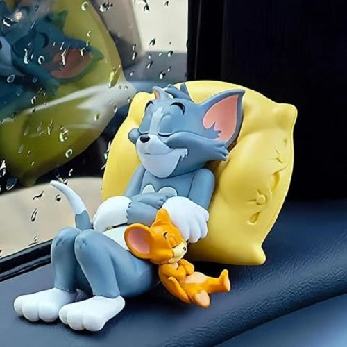 Tom and Jerry dashboard toy figurine featuring a sleeping Tom cat on a yellow pillow with Jerry mouse nestled beside him, resting on a car dashboard with rain on the window. A cute PVC cartoon car accessory.