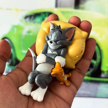 A person's hand holding a small sleeping Tom and Jerry action figure for car, demonstrating the compact size of the PVC dashboard toy. A bright green car is visible in the blurred background.