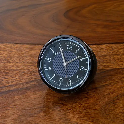 Detailed front view of the universal mini auto clock resting on a wooden surface, highlighting its classic analog display, easy-to-read numbers, and compact design.